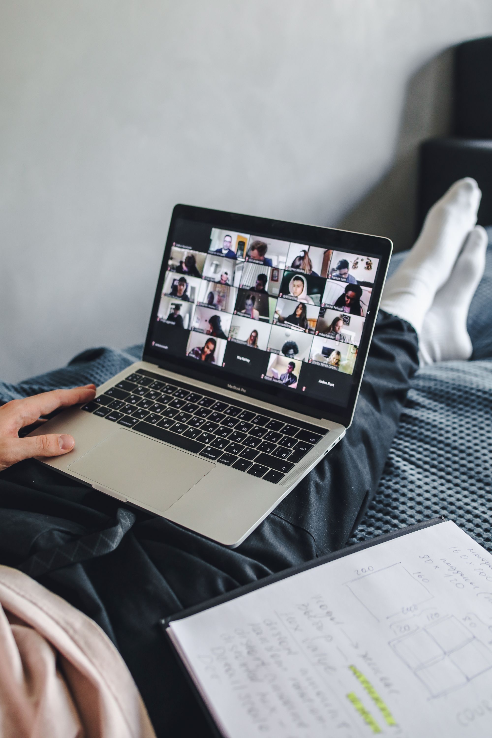 Laptop showing a video call grid with a handwritten notebook open in the foreground